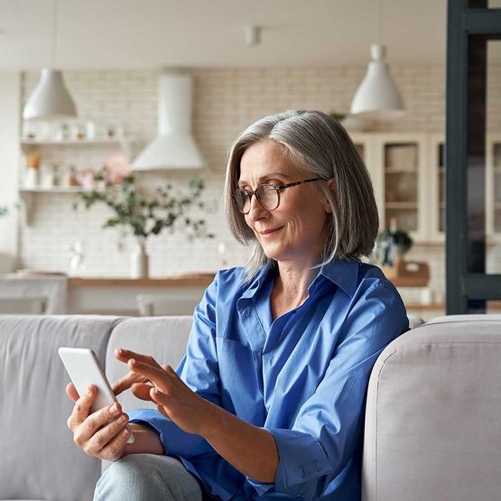 Entspannte reife alte 60er-Jahre-Frau, ältere Kundin mittleren Alters, die Smartphone mit mobiler App hält, SMS-Nachricht sendet, E-Commerce-Angebote auf Handy-Technologie-Geräten durchsucht, die zu Hause auf der Couch sitzen.